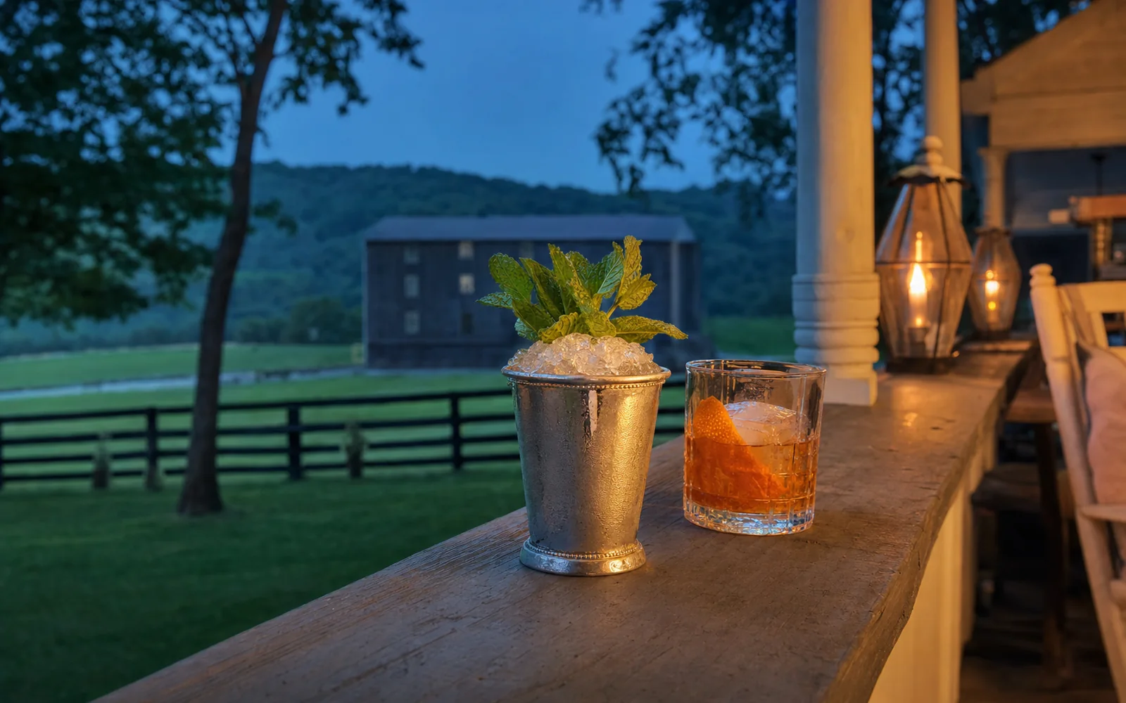 Frosted silver julep cup packed with crushed ice and fresh mint beside an Old Fashioned on a porch railing at dusk, AI-generated illustration