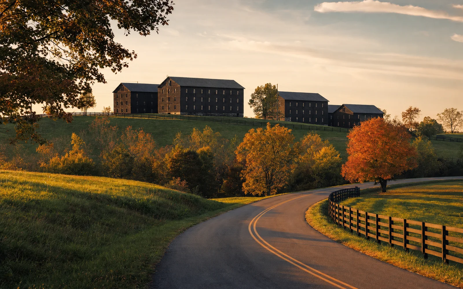 Tall dark rickhouses on a rolling Kentucky hillside at sunset, with fall trees and a two-lane road in the foreground, AI-generated illustration