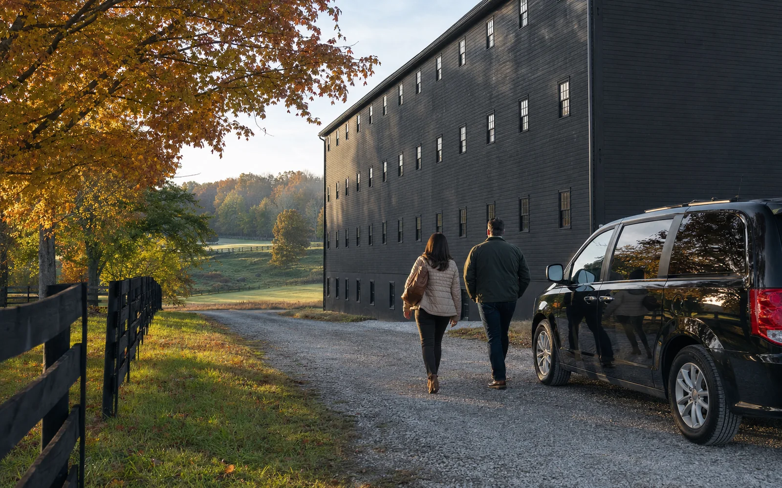 Black passenger van parked on a gravel lane beside a tall dark rickhouse on a clear autumn morning, AI-generated illustration
