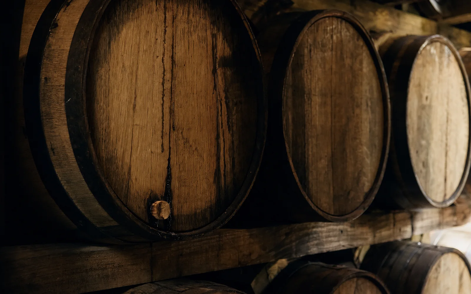 Close view of oak barrel heads stacked in a rickhouse, their charred edges and iron hoops lit by a warm side light, AI-generated illustration