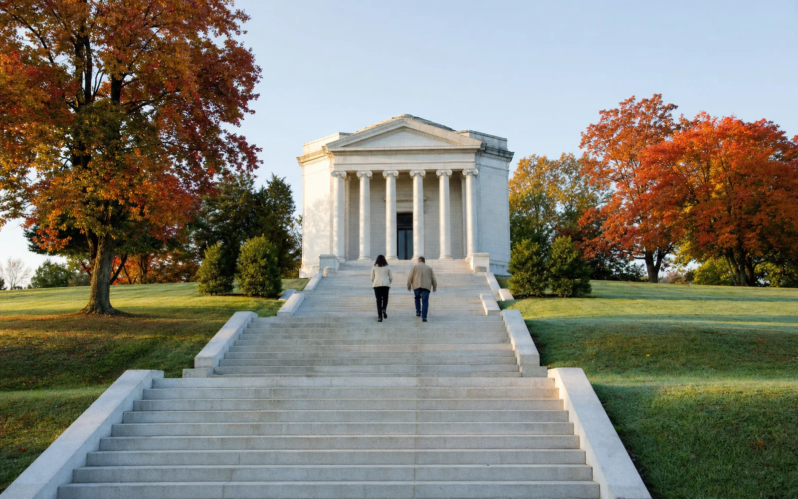 White granite neoclassical memorial with columns at the top of a long flight of stone steps, framed by autumn trees in morning light, AI-generated illustration