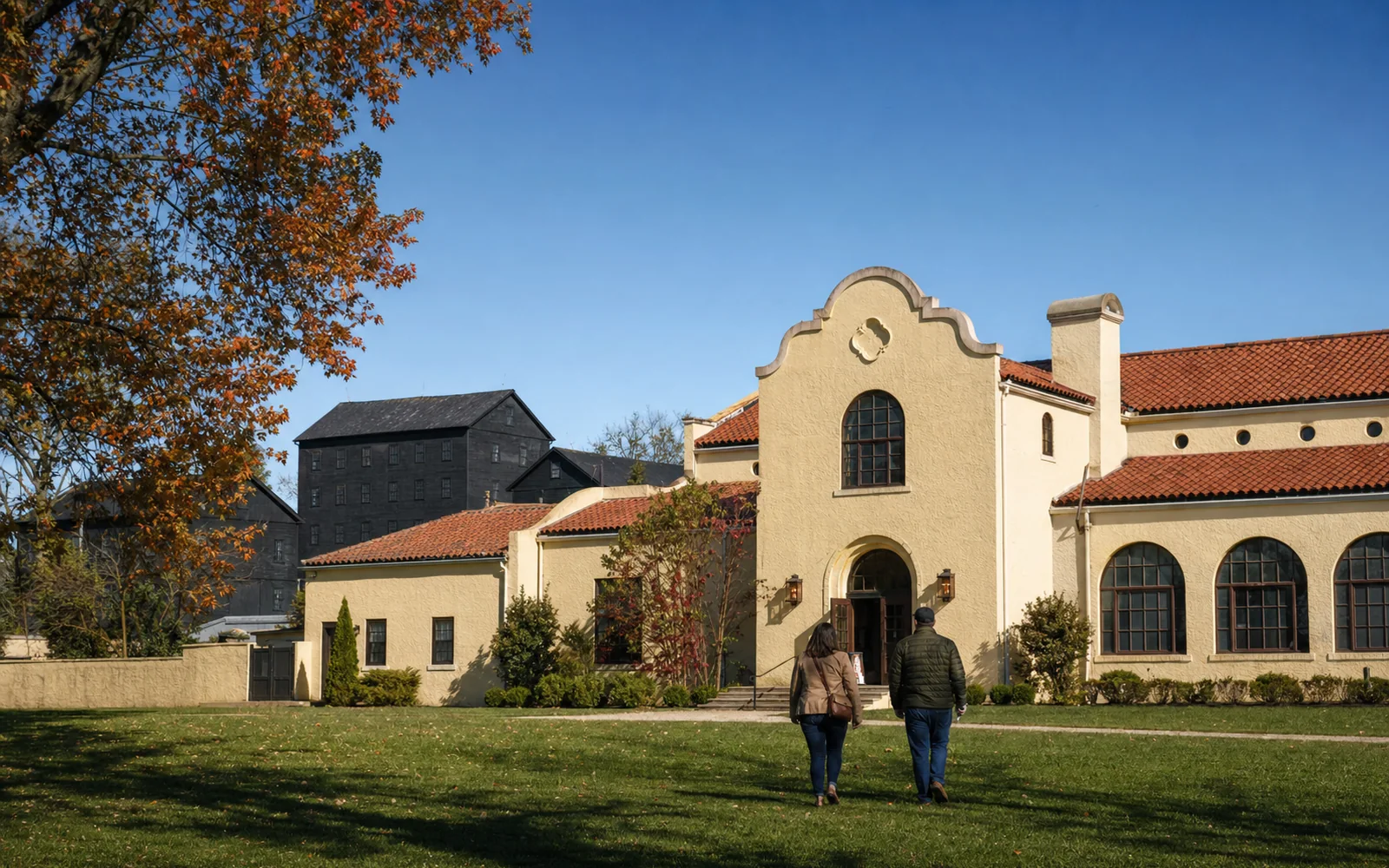Spanish Mission-style distillery buildings with pale stucco walls and red tile roofs under a clear autumn sky, AI-generated illustration