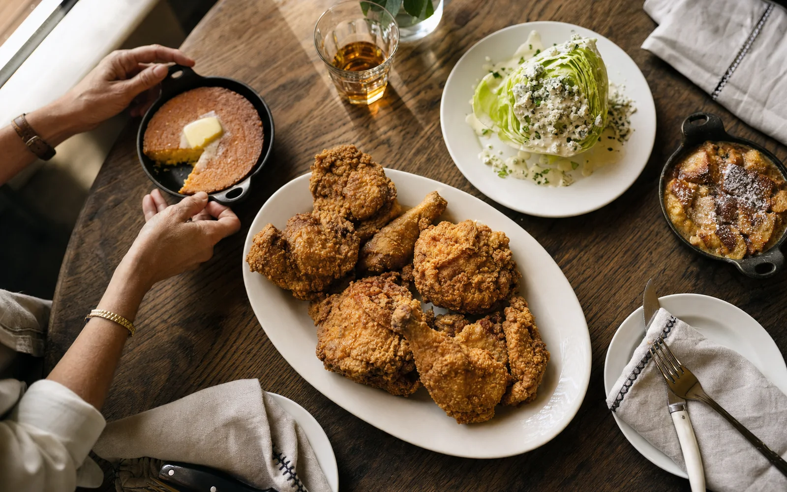 A dinner table with skillet-fried chicken, cast-iron cornbread, a wedge salad and a glass of bourbon under warm light, AI-generated illustration