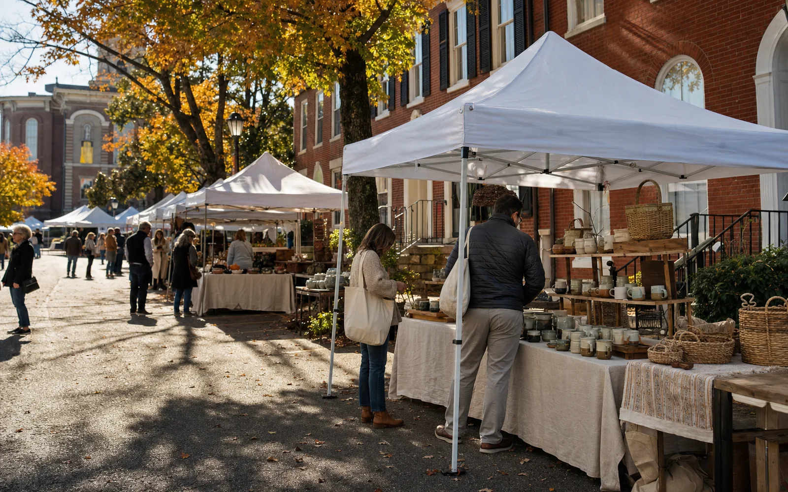 Rows of white vendor tents along a tree-lined brick street in autumn with handmade pottery on display tables, AI-generated illustration