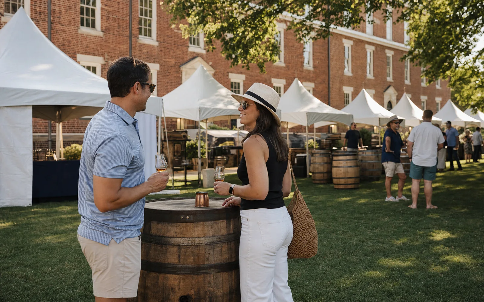 White festival tents on a green lawn in front of a tall red brick college building on a sunny September afternoon, adults holding tasting glasses, AI-generated illustration