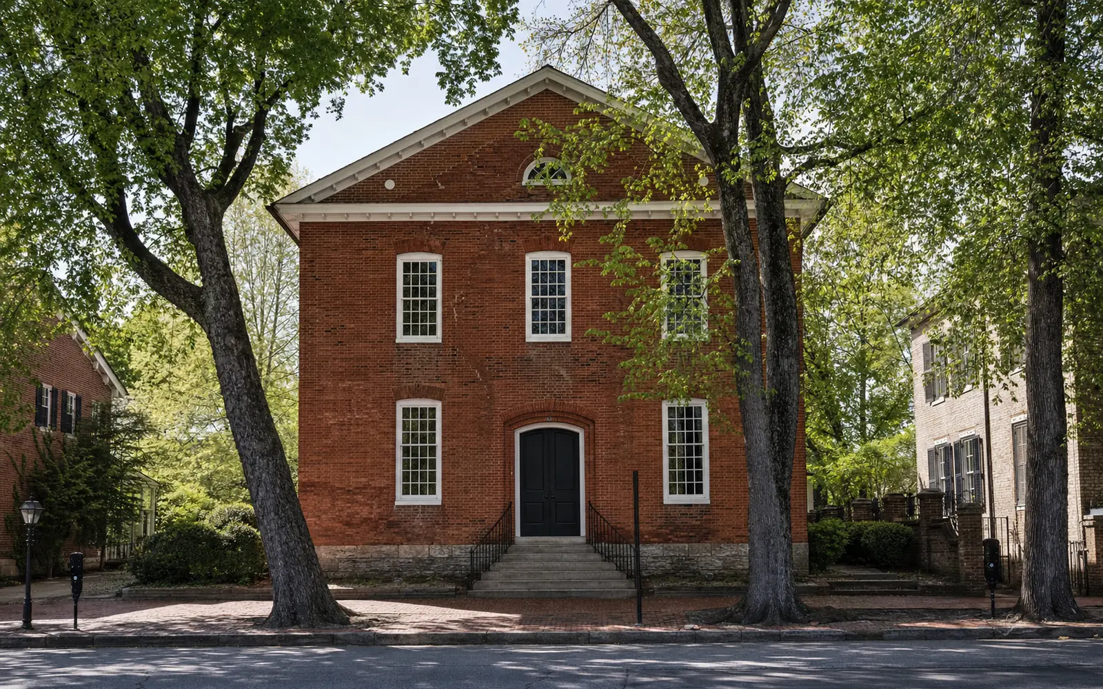 Two-story early 19th-century red brick church with a simple gabled front and tall windows on a quiet tree-lined small-town street in spring, AI-generated illustration
