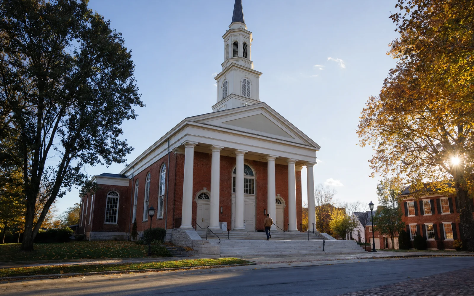 Greek Revival brick church with a white columned portico and tall steeple against a clear blue autumn sky, AI-generated illustration