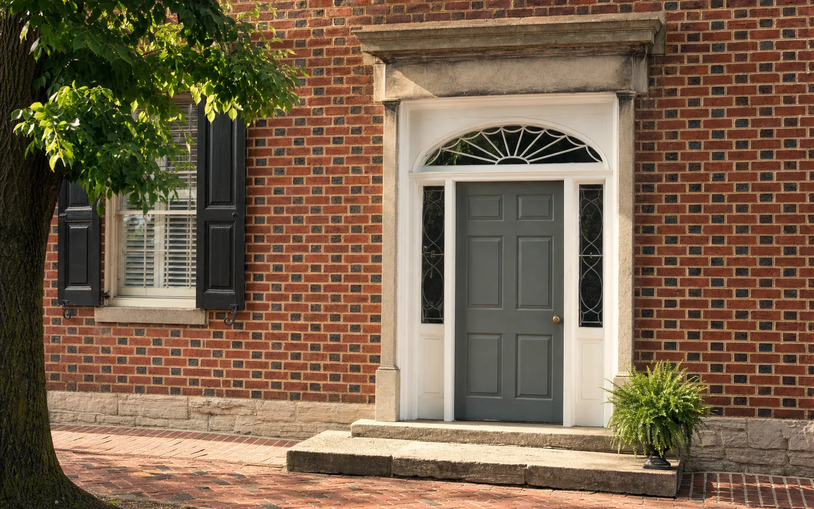 Close view of a Federal-style brick doorway with a semicircular fanlight, paneled door and limestone steps on a quiet street, AI-generated illustration