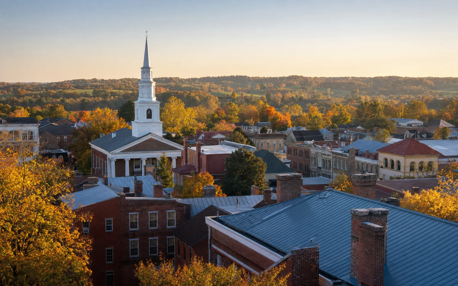 Elevated view over the brick rooftops of a small historic town with a white church steeple rising among autumn trees, AI-generated illustration