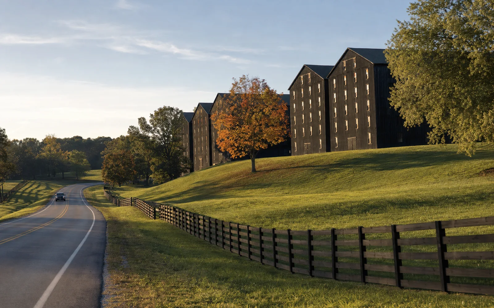 Two-lane Kentucky highway curving past dark bourbon warehouses and green fields under a clear autumn sky, AI-generated illustration