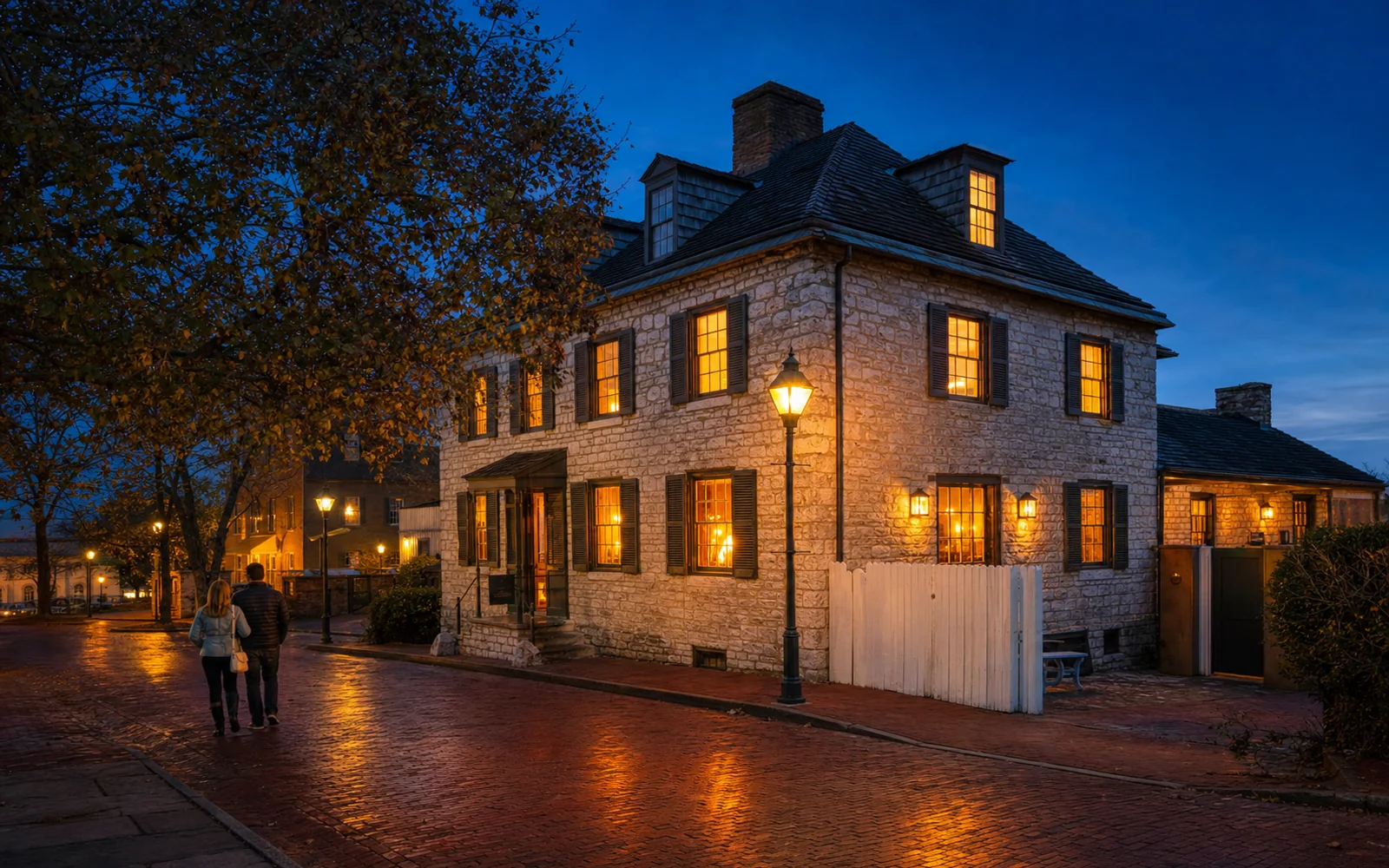 Old stone tavern on a brick town square at blue hour, warm light glowing from small-paned windows and a couple walking past, AI-generated illustration